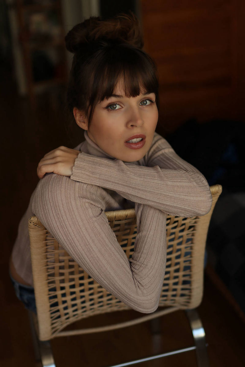Portrait von einer jungen Frau, die auf einem Stuhl sitzt.